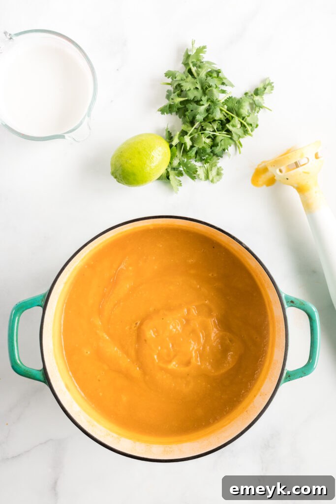 Curried Butternut Squash Soup simmering in a large pot on the stovetop, showing the bright orange color of the squash.