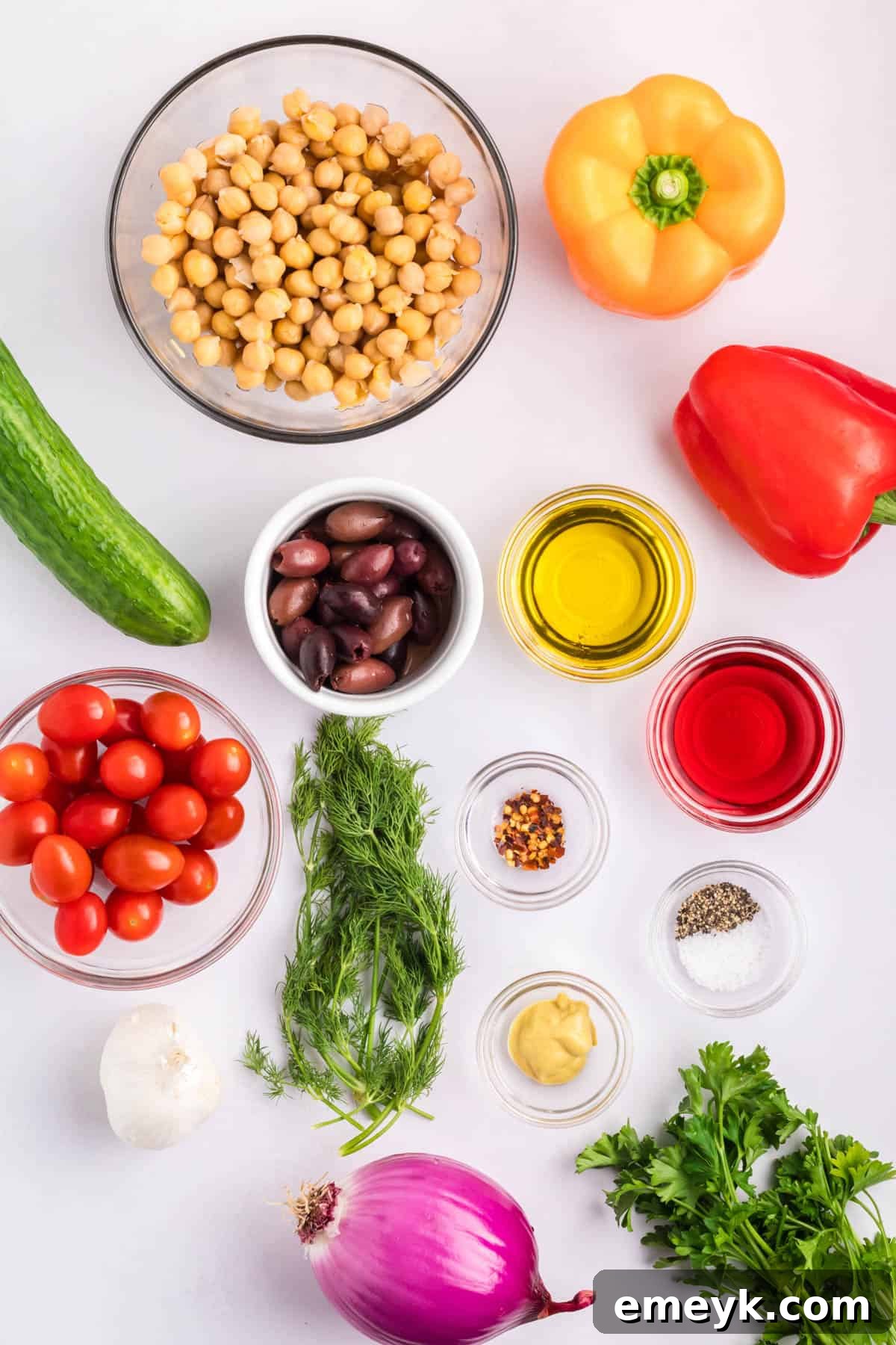 Mediterranean Chickpea Salad ingredients laid out on a table, including canned chickpeas, fresh vegetables, herbs, and dressing components