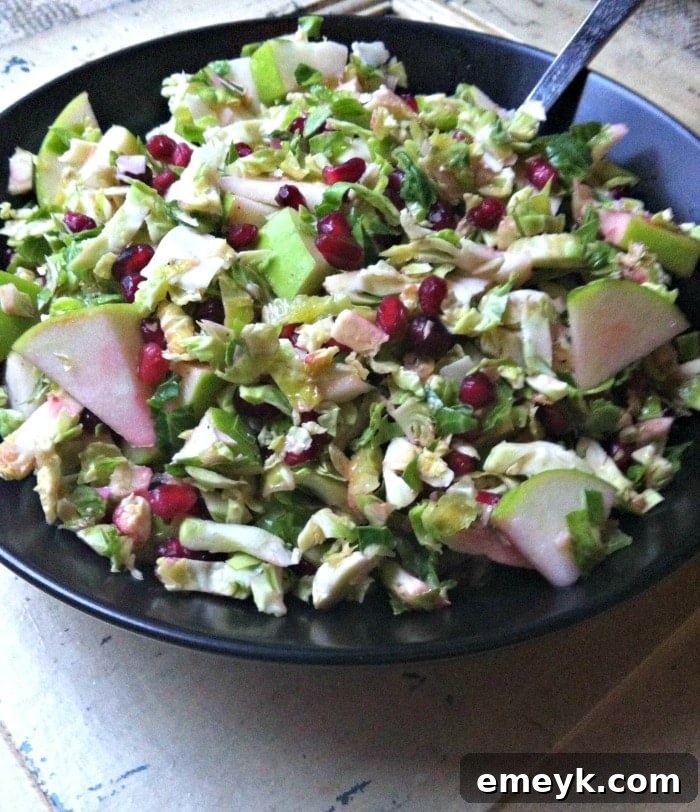 A bowl of delicious Shaved Brussels Sprout Salad featuring a mix of green Brussels sprouts, red pomegranate, and white cheese, ready to be served.