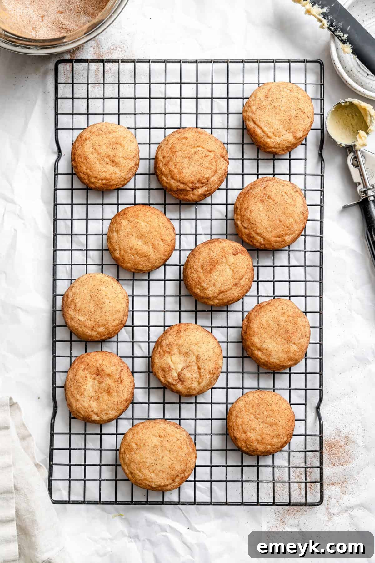 Easy Snickerdoodle Recipe freshly baked cookies on a baking sheet, with a few already moved to a cooling rack.