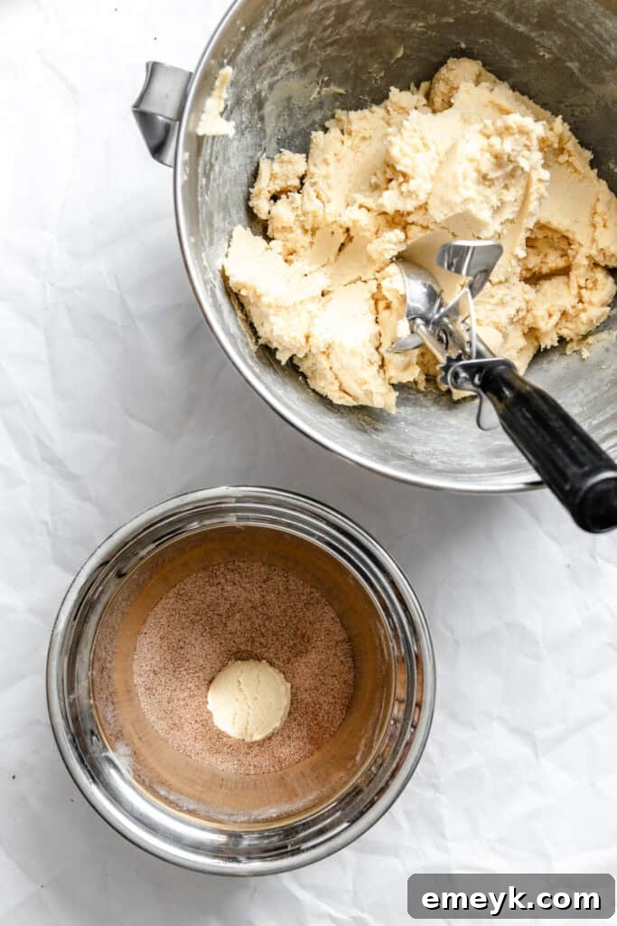 Easy Snickerdoodle Recipe showing a ball of cookie dough being rolled in cinnamon sugar mixture.