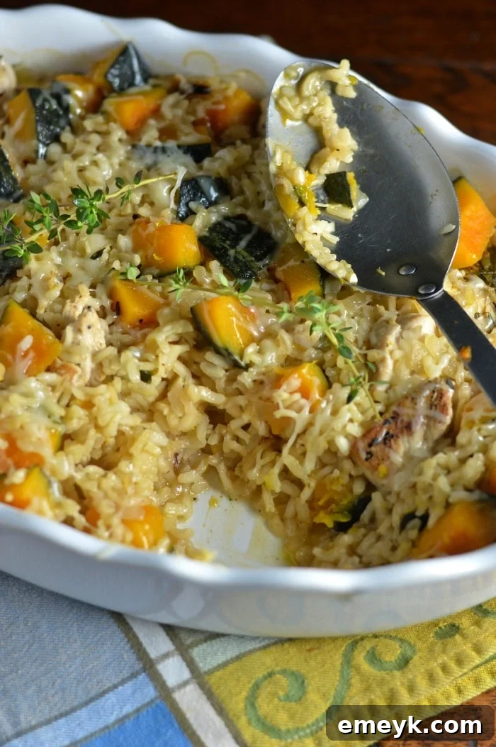 A close-up of Baked Chicken Kabocha Squash Risotto Recipe in a white dish with a spoon, showing the creamy texture and pieces of chicken and squash.