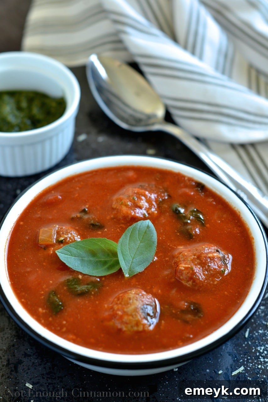 A close-up of Spinach and Tomato Soup with a spoon, showing the rich texture and meatballs.