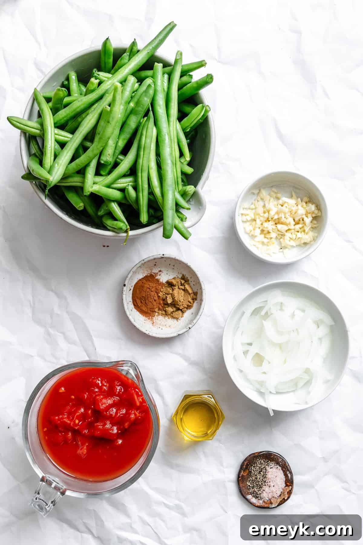A selection of fresh ingredients including green beans, diced tomatoes, onion, garlic, and spices, laid out for Lebanese Green Beans