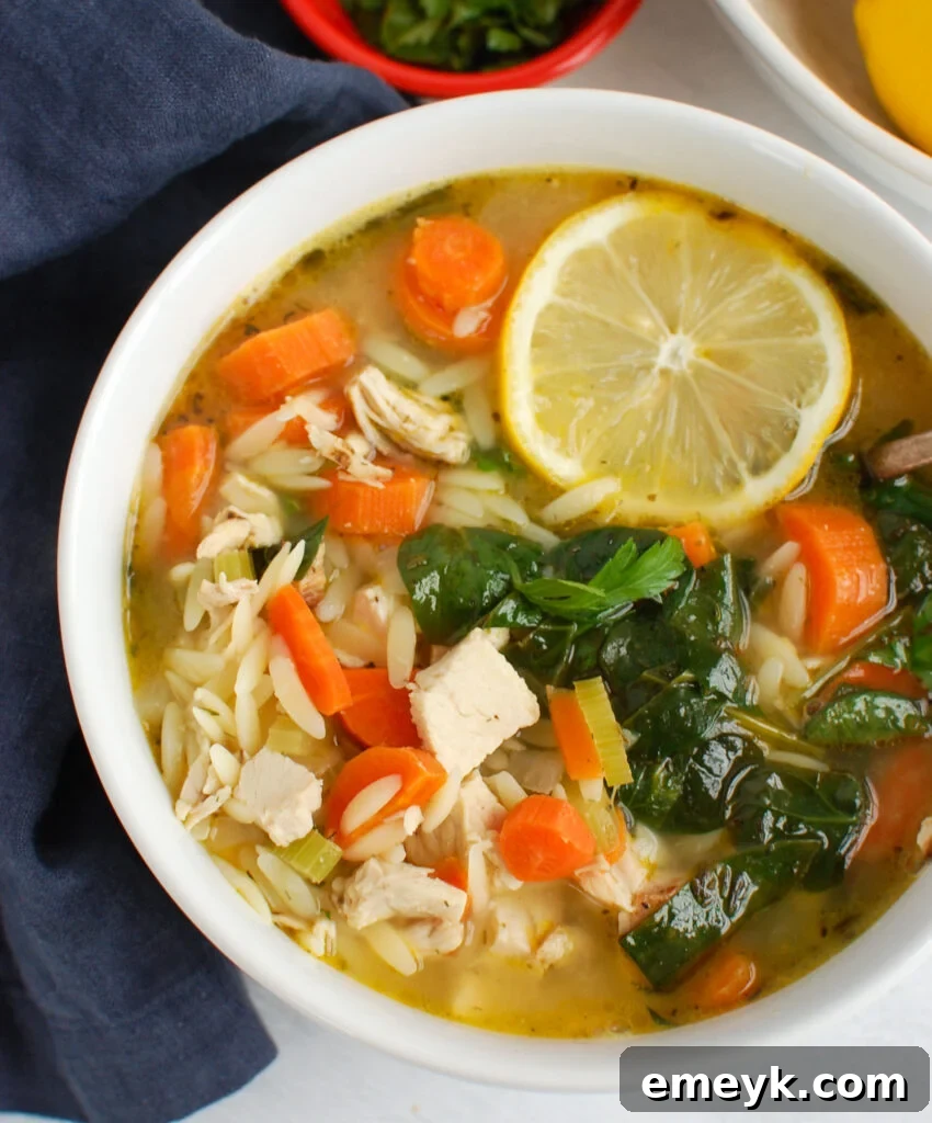Lemon Chicken Orzo Soup in white bowl with a spoon, garnished with fresh herbs