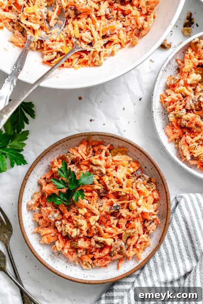 Golden Carrot Raisin Delight 3 Two aesthetically arranged small bowls of Carrot Raisin Salad, freshly prepared and ready to serve, highlighting the vibrant colors and appealing textures of the combined ingredients.