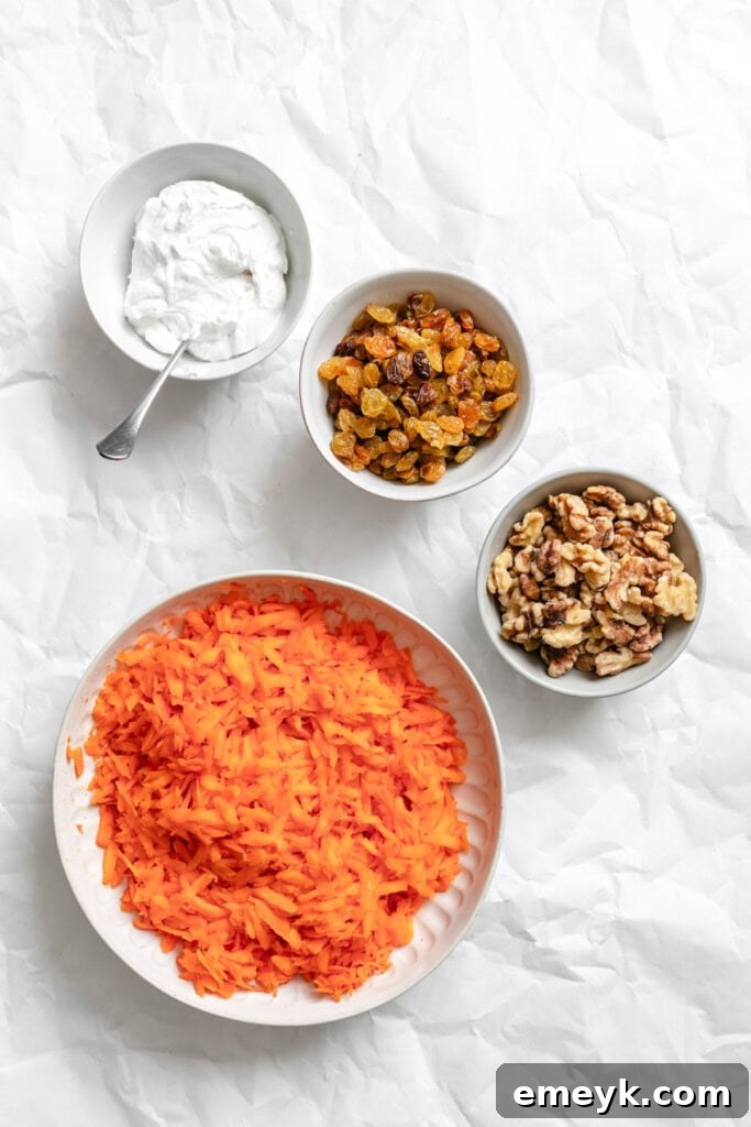 Golden Carrot Raisin Delight 6 A vibrant close-up of the fresh, essential ingredients for Carrot Raisin Salad, including a generous pile of finely shredded carrots, a bowl of plump golden raisins, crunchy walnut halves, and creamy plain yogurt, neatly arranged on a rustic wooden cutting board.