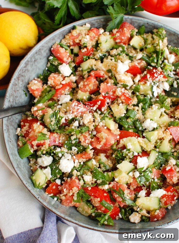 Close-up of a vibrant Tomato Cucumber Feta Quinoa Salad in a bowl with a spoon, highlighting the fresh ingredients.