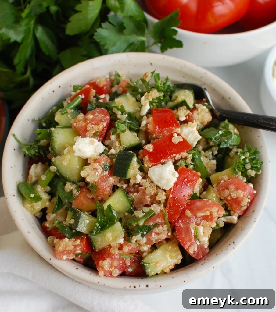 A small serving of Tomato Cucumber Feta Quinoa Salad in a glass bowl, garnished with fresh herbs.