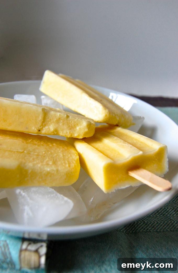 A close-up of a perfectly frozen Pina Colada Popsicle in a clear mold, showcasing its creamy texture and tropical fruit specks, ready to be enjoyed.