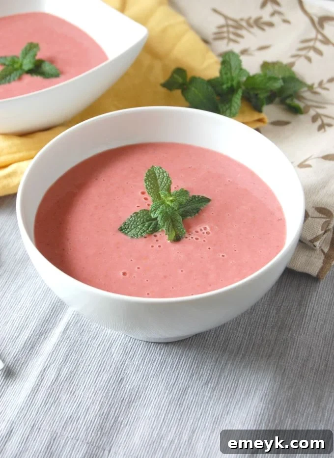 Vibrant Strawberry Mint Gazpacho garnished with fresh mint leaves in a white bowl, perfect for a summer day.