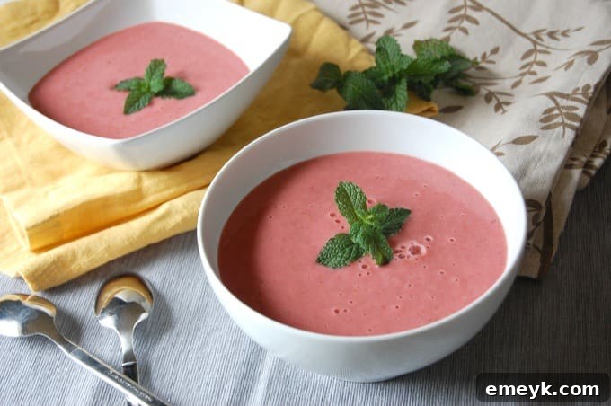 Close-up of Strawberry Mint Gazpacho in a modern white bowl, garnished with a fresh mint sprig.