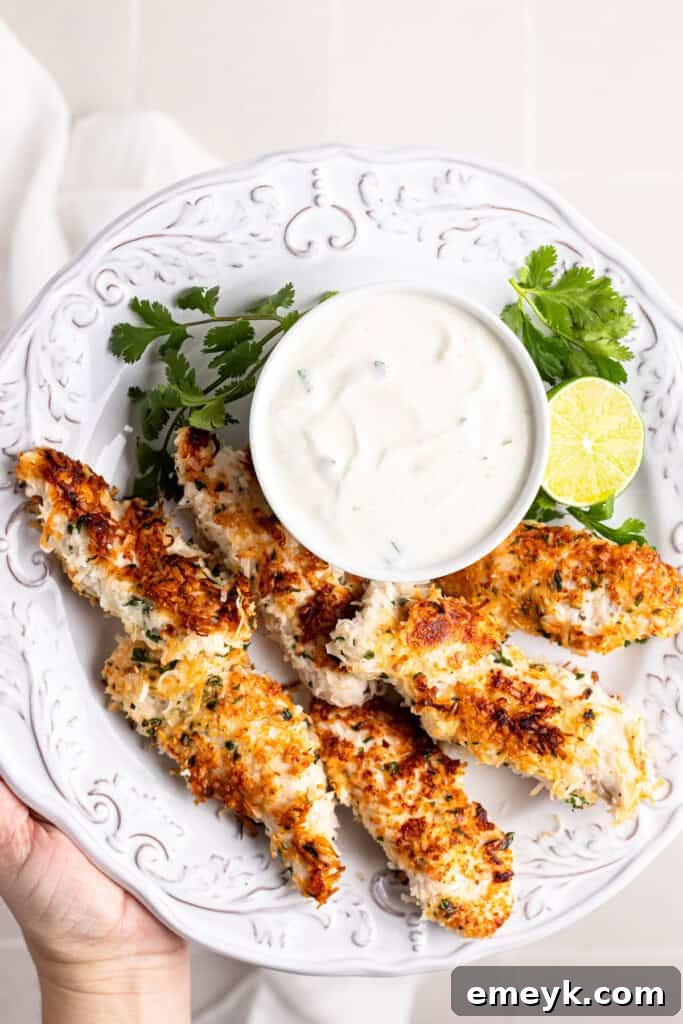 Crispy Coconut Chicken Tenders served on a white plate with a side of cilantro lime dip and fresh lime wedges.