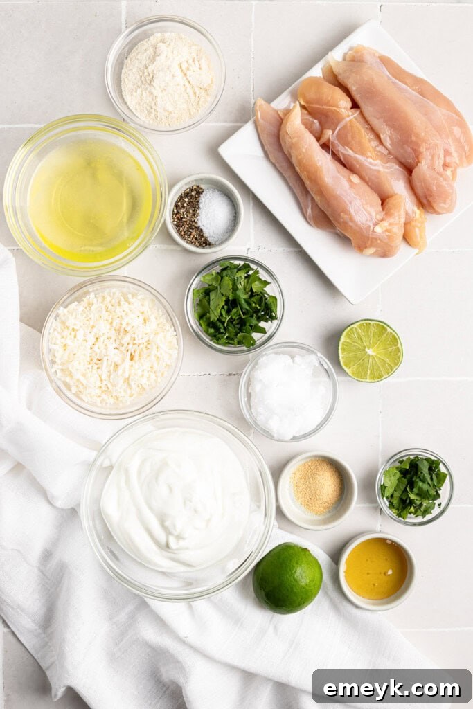 Golden Crispy Baked Coconut Chicken Tenders Kids Love 3 Ingredients for Coconut Chicken Tenders laid out on a wooden board: chicken tenderloins, coconut flour, shredded coconut, eggs, lime, cilantro, and Greek yogurt.