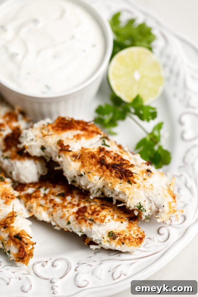 Golden Crispy Baked Coconut Chicken Tenders Kids Love 4 A close-up of Crispy Coconut Chicken Tenders on a white plate, garnished with fresh cilantro.