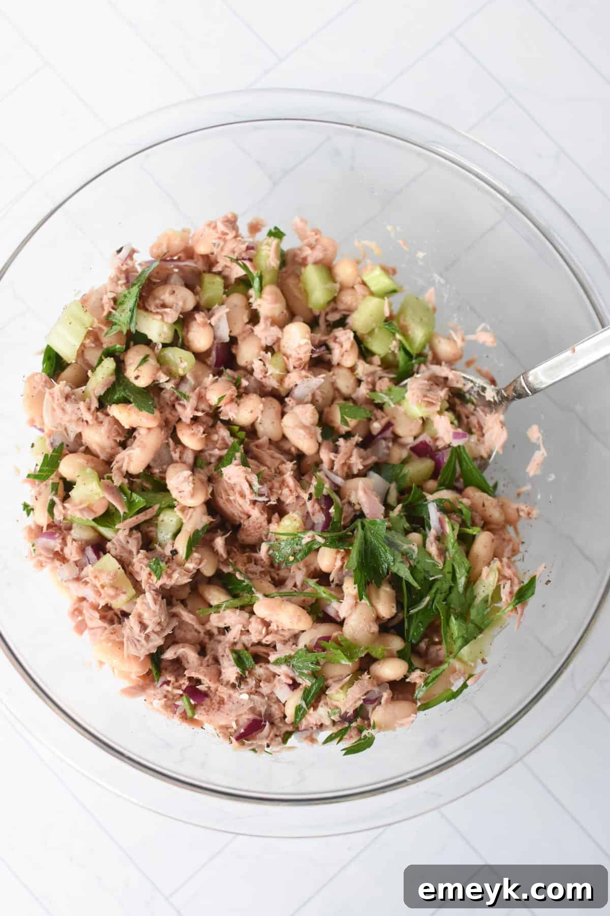Step 2: Drizzling lemon juice and olive oil over the tuna and bean mixture in a clear bowl.