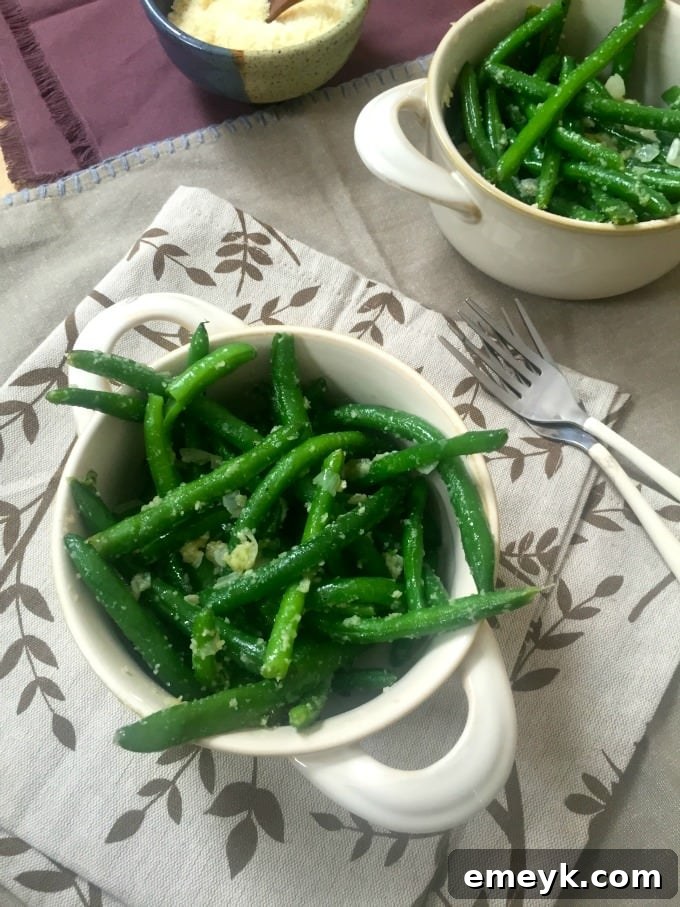 A vibrant bowl of green beans generously topped with freshly grated Parmesan cheese, glistening and ready to serve.