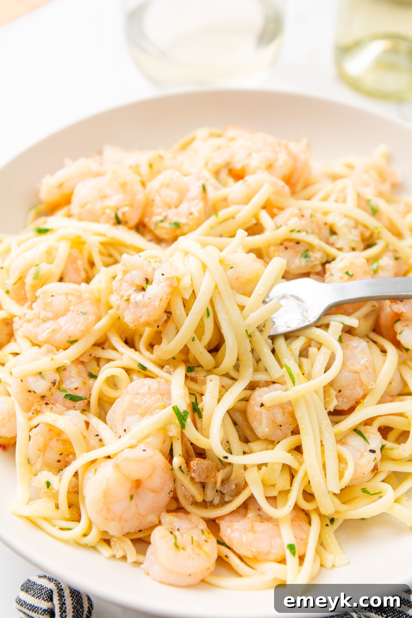 Close-up of Lemon Garlic Shrimp Pasta on a white plate with a fork, showcasing the perfectly cooked shrimp and linguine.