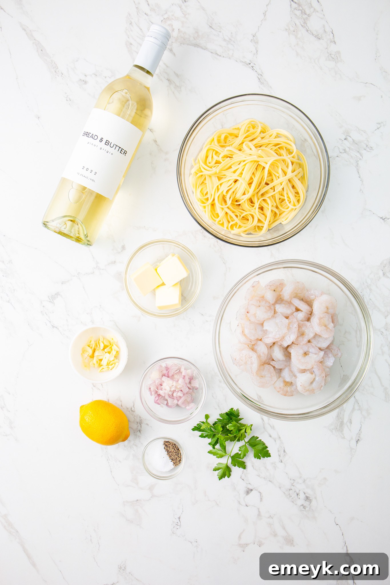 All ingredients for Lemon Garlic Shrimp Pasta laid out on a wooden cutting board: pasta, shrimp, lemons, garlic, parsley, butter, and white wine.
