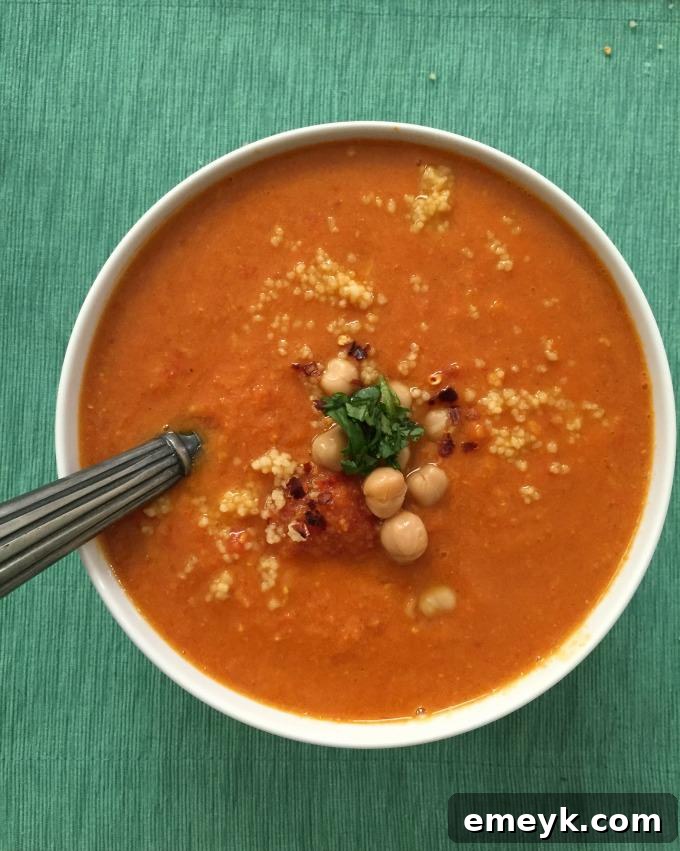 Cooked Moroccan Tomato Couscous Chickpea Soup being poured into a serving bowl, showcasing its chunky ingredients.