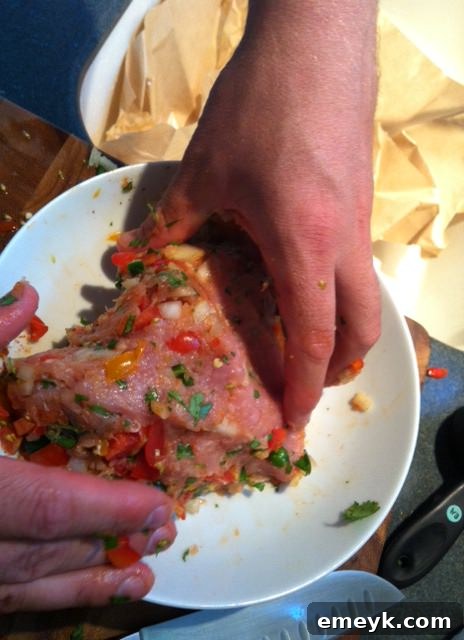 A person's hands gently mixing ground turkey with the colorful vegetable and spice mixture in a bowl