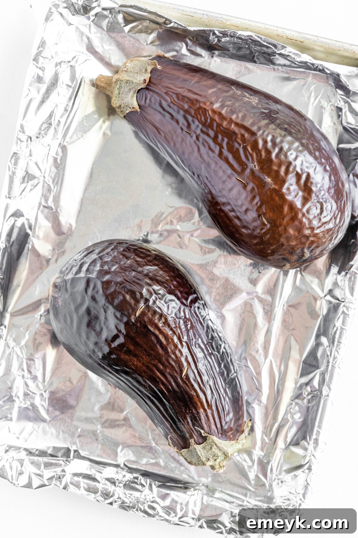 Roasted eggplants with shriveled skin on a baking sheet, ready for Baba Ghanoush preparation.
