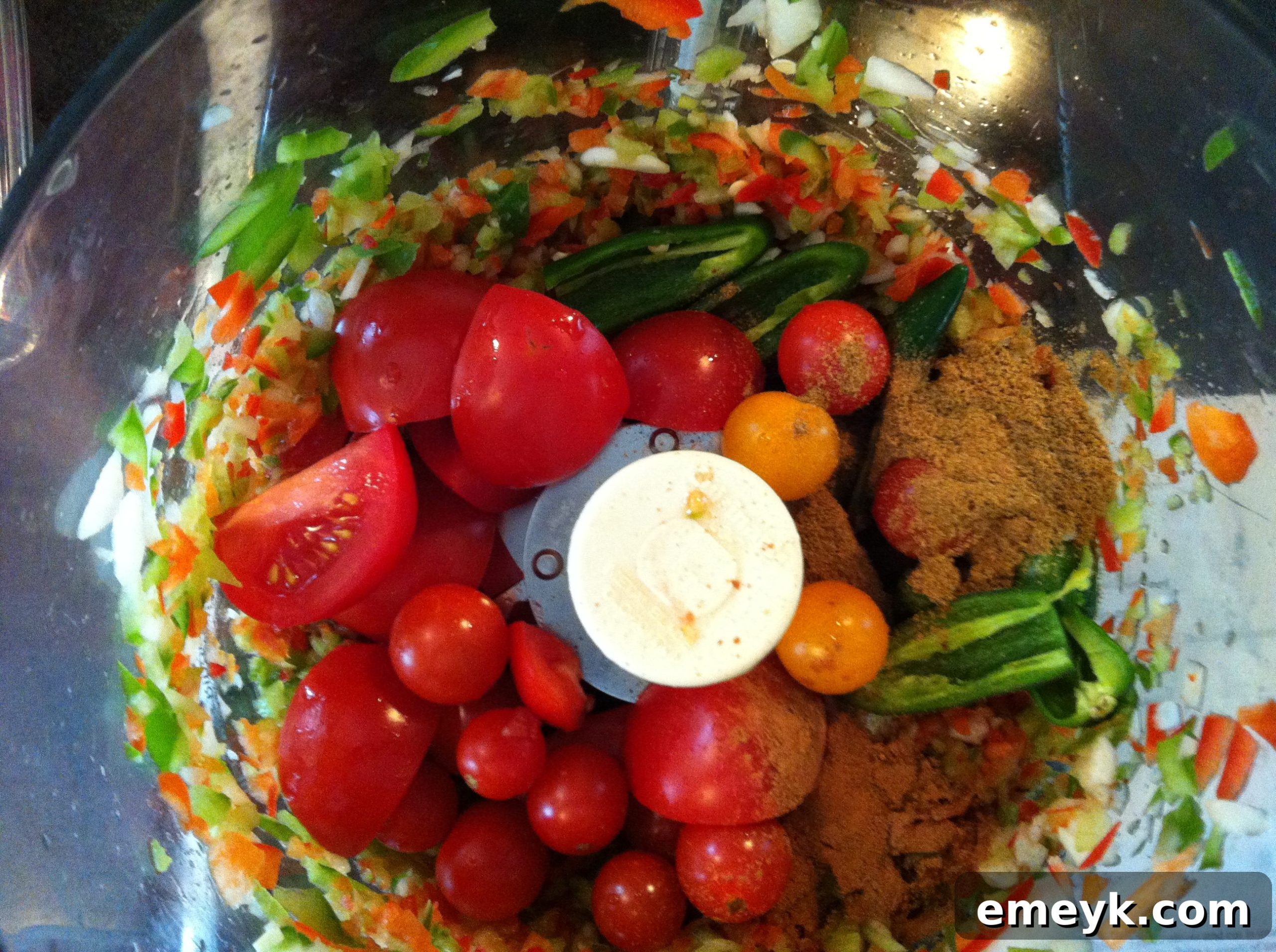Diced tomatoes being added to other fresh ingredients in a food processor for salsa.