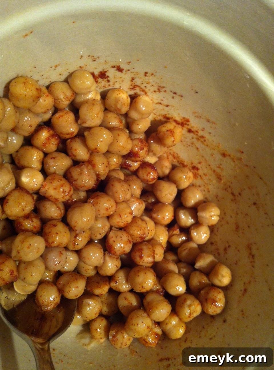 Chickpeas in a bowl, coated with olive oil, cayenne pepper, and salt, perfectly seasoned for roasting.