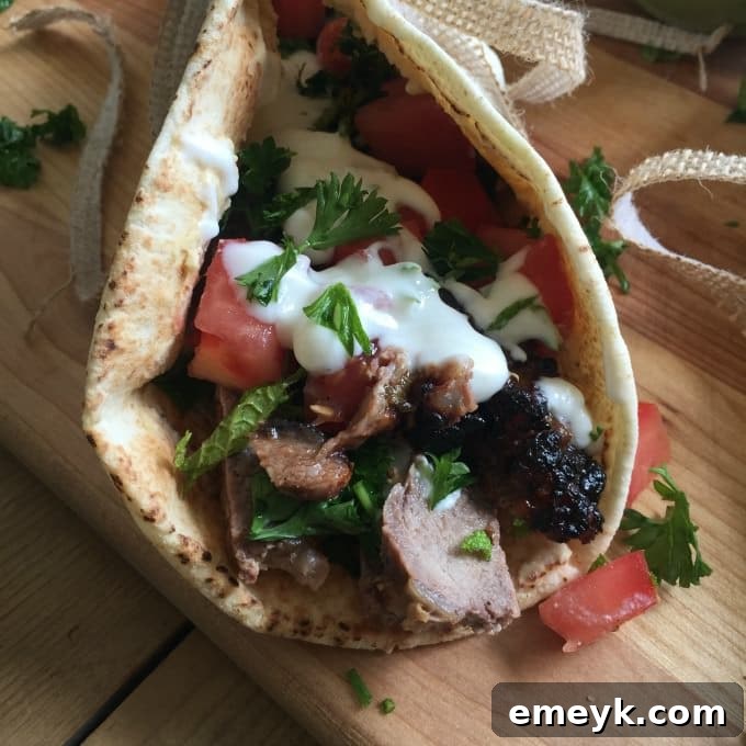 Grilled Mediterranean Steak Pita Wrap with Mint Yogurt Sauce, fresh tomatoes, and parsley on a wooden cutting board.