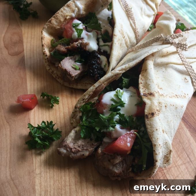 Close-up of a sliced Mediterranean Steak Pita Wrap, showcasing layers of grilled steak, lemon hummus, mint yogurt sauce, and fresh toppings.