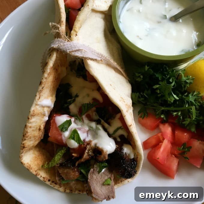 A Mediterranean Steak Pita Wrap on a white plate, garnished with fresh mint and served alongside extra mint yogurt sauce.