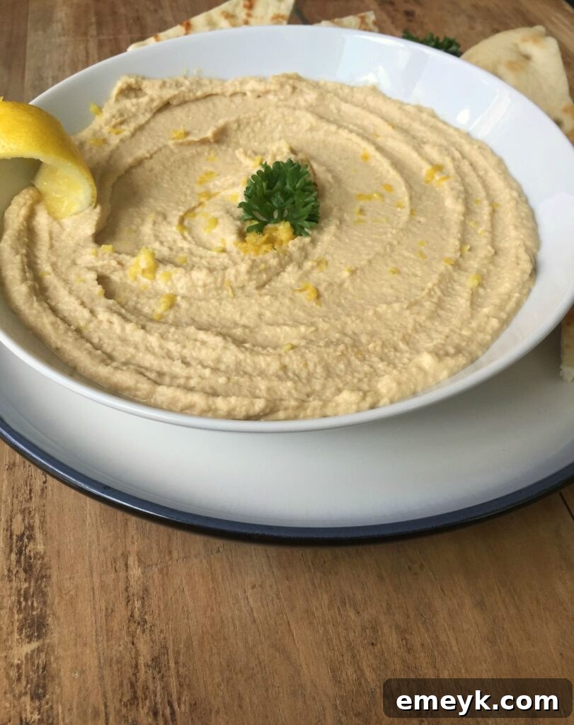 A bowl of vibrant Lemon Hummus garnished with fresh parsley and lemon slices on a rustic wooden board.