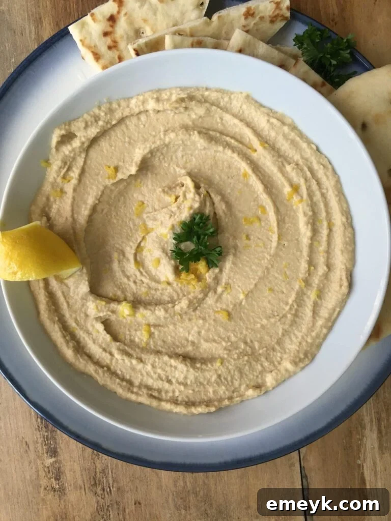 A close-up of creamy lemon hummus with a half lemon slice on the side, ready to be served.