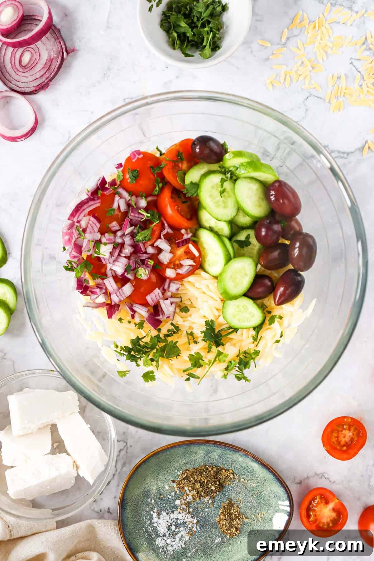 A large mixing bowl filled with Greek Orzo Pasta Salad ingredients before dressing is added.