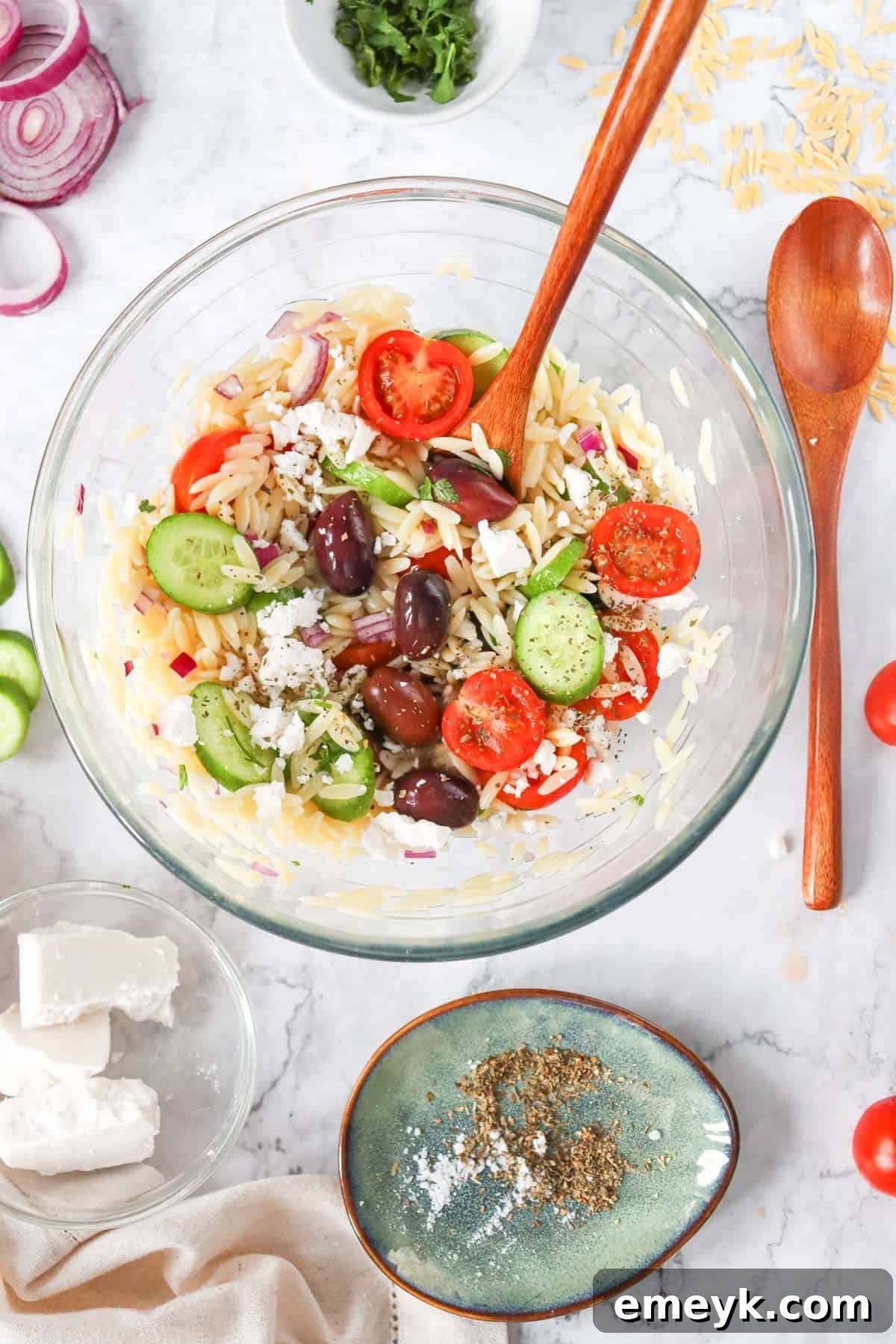 A white bowl of Greek Orzo Pasta Salad with a serving spoon, ready to be eaten.