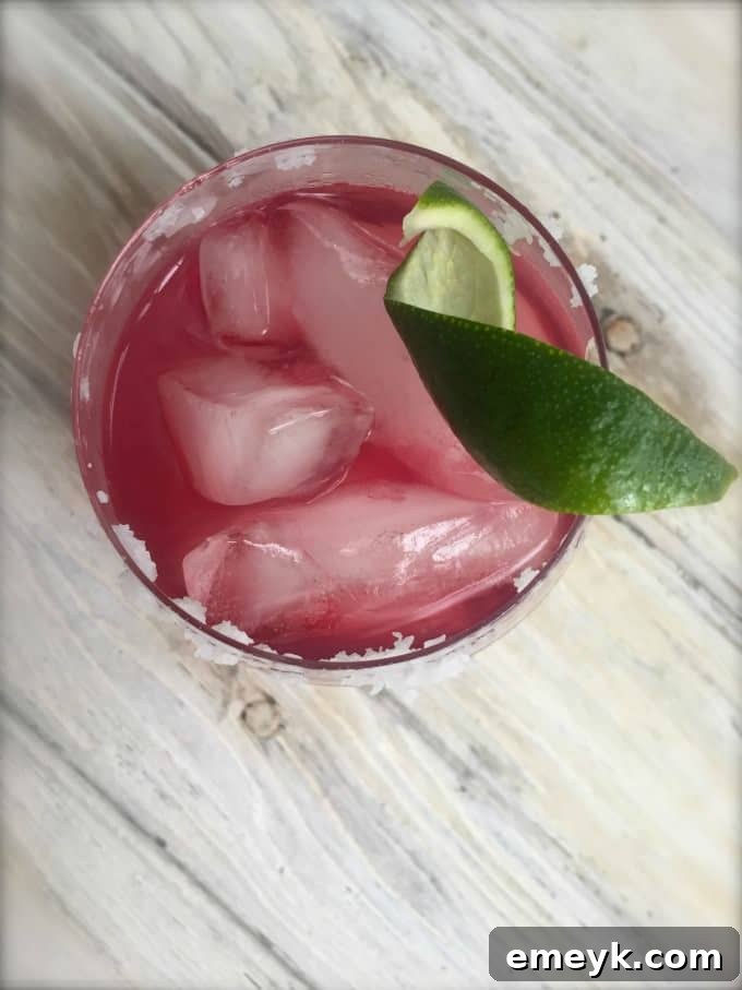 Ruby Pomegranate Margarita 2 Pomegranate Margarita - A beautiful red cocktail in a salt-rimmed glass, garnished with lime.