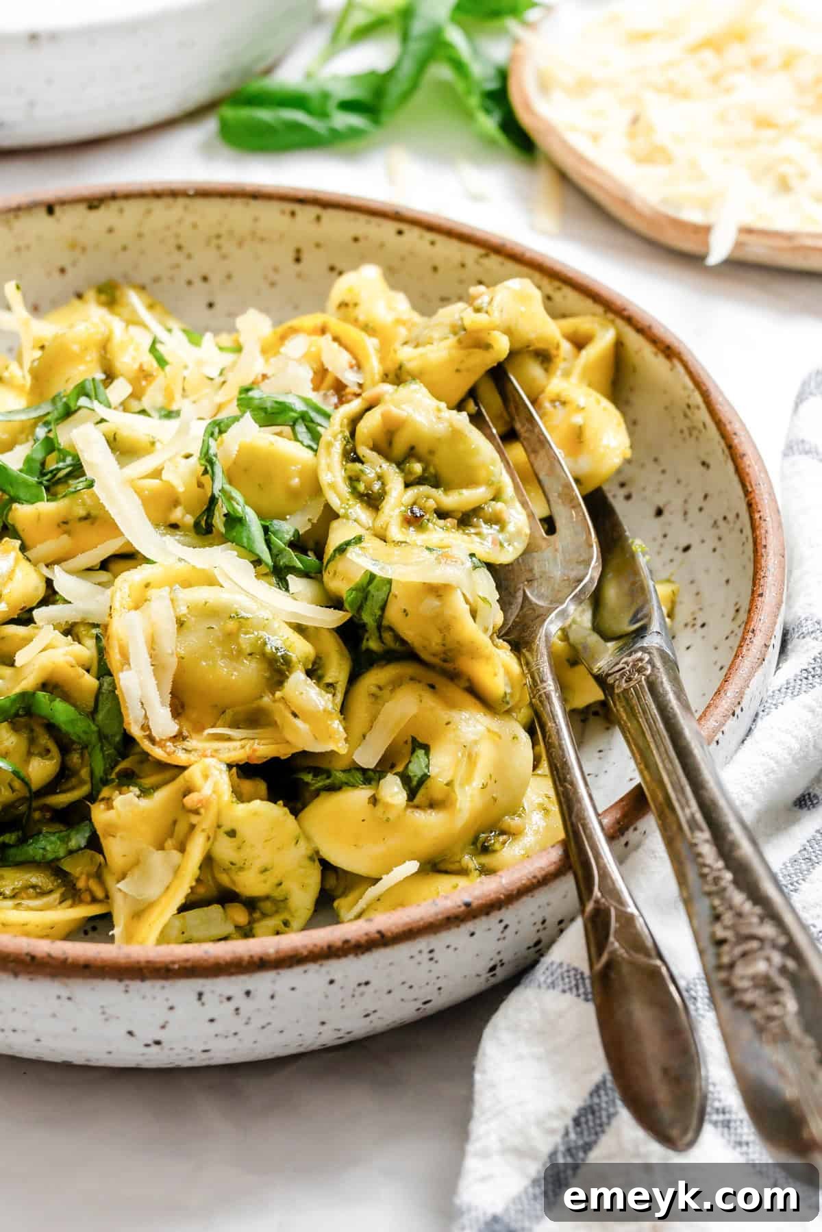 A delectable bowl of pesto tortellini, garnished with fresh basil, ready to be enjoyed, with a fork and knife resting beside it.