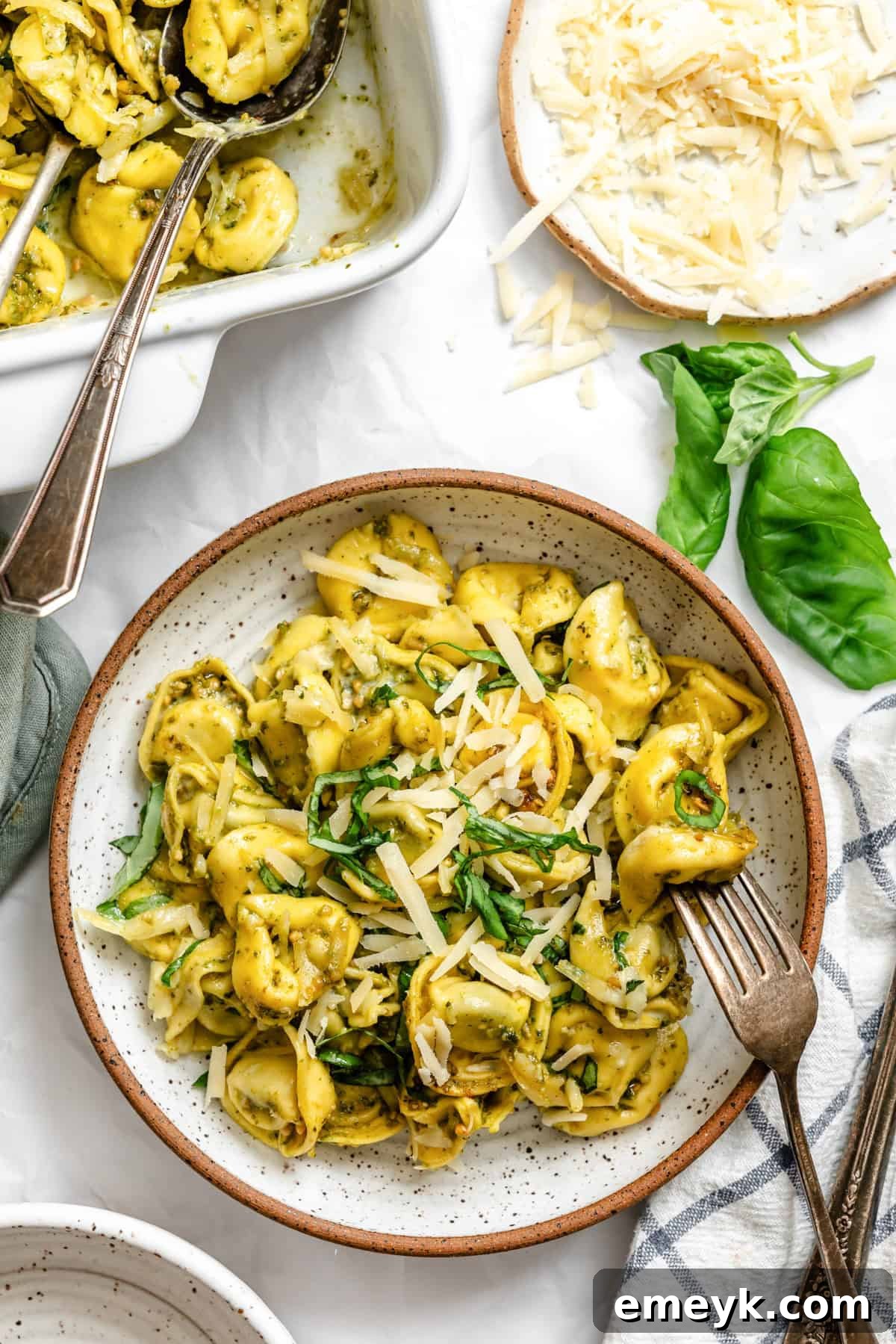 A serving of baked pesto tortellini in a white bowl, garnished with fresh basil leaves.