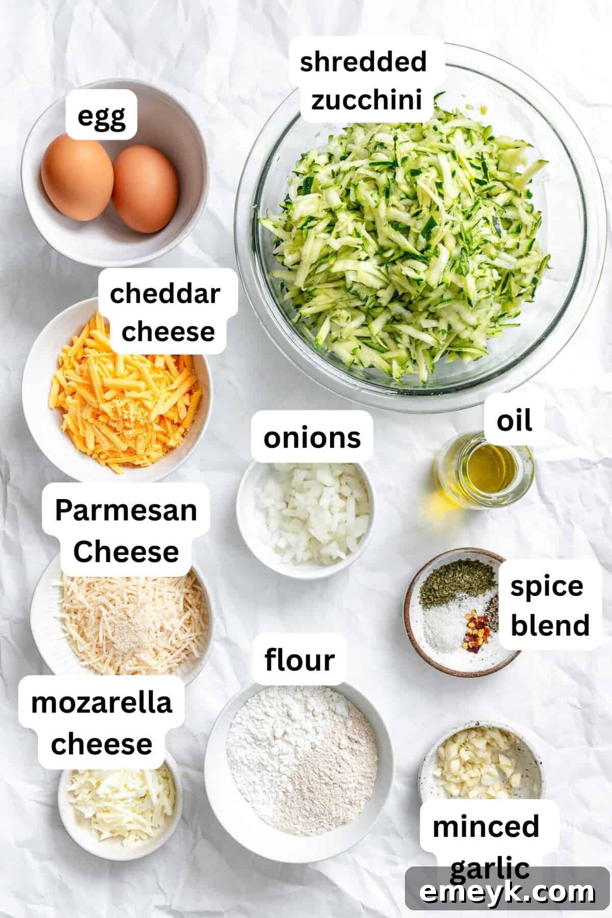 A collection of fresh ingredients laid out for Easy Zucchini Fritters, including grated zucchini, eggs, cheeses, and spices.