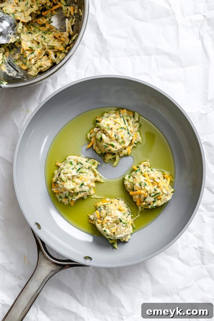 Zucchini fritters sizzling in a hot pan, cooking to a perfect golden-brown.