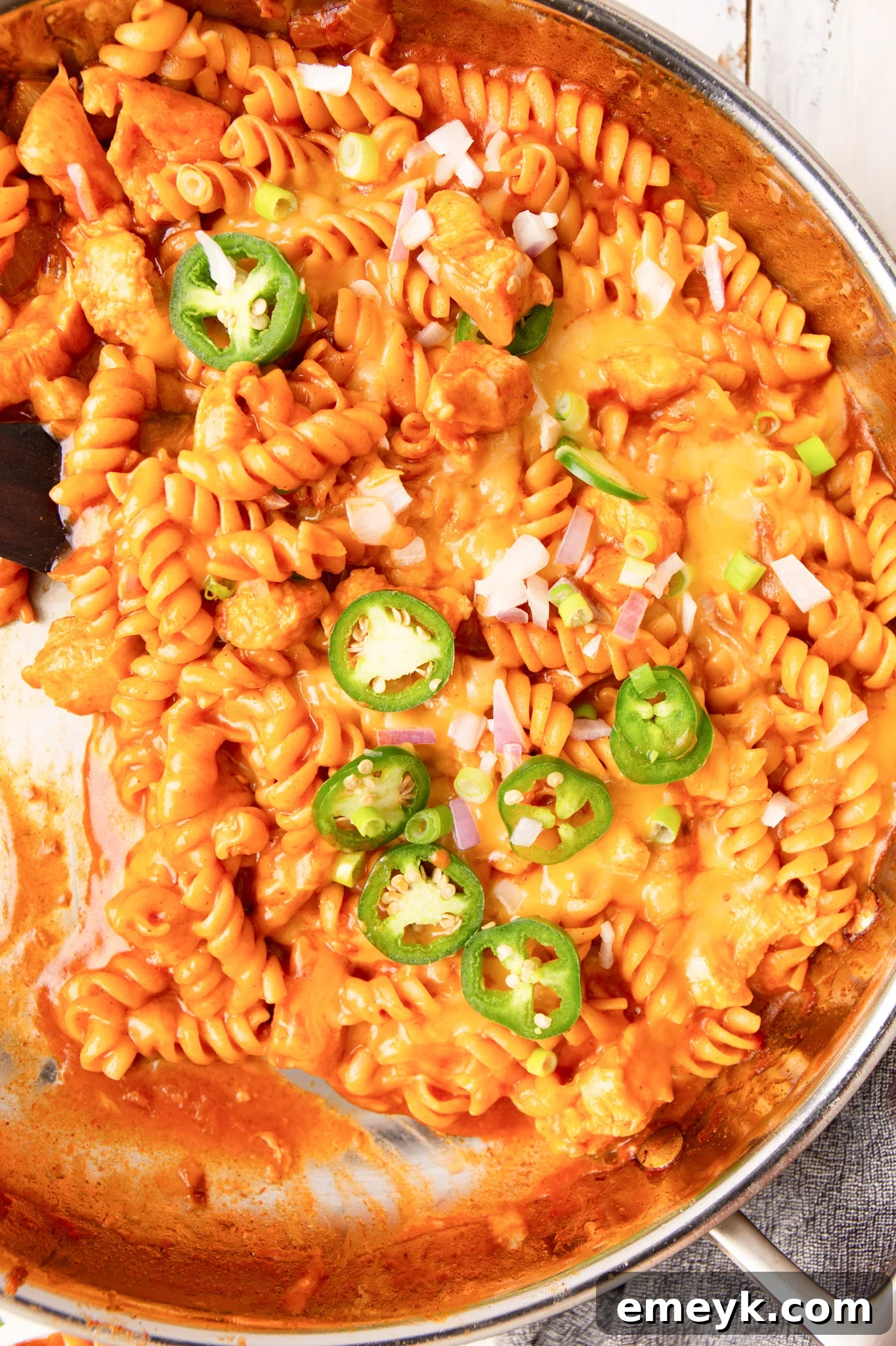 A large pot filled with creamy One Pot Chicken Enchilada Pasta, garnished with fresh cilantro and red onion, ready to be served.