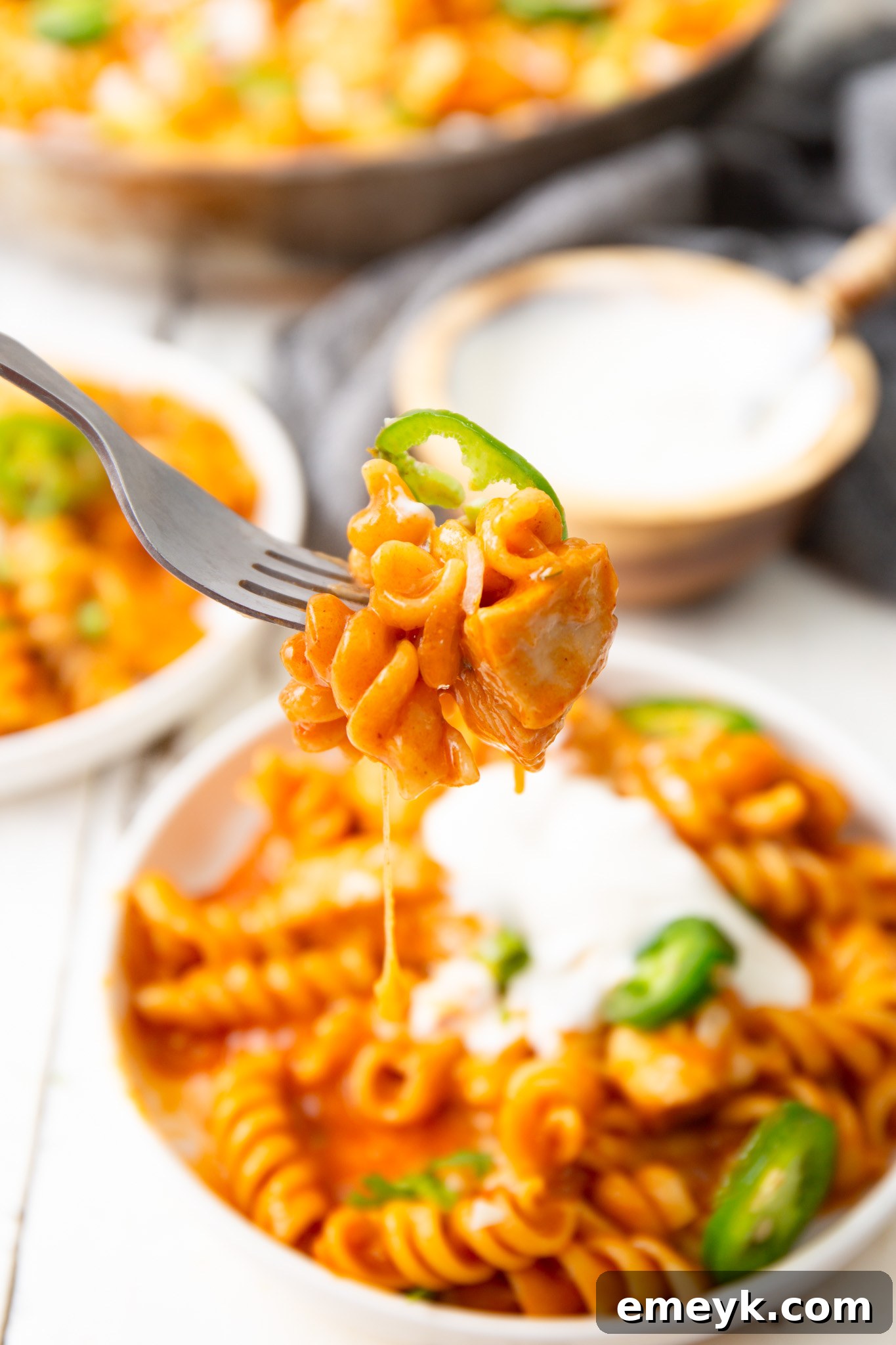 A fork lifting a delicious bite of One Pot Chicken Enchilada Pasta, showing the tender chicken, pasta, and melted cheese.