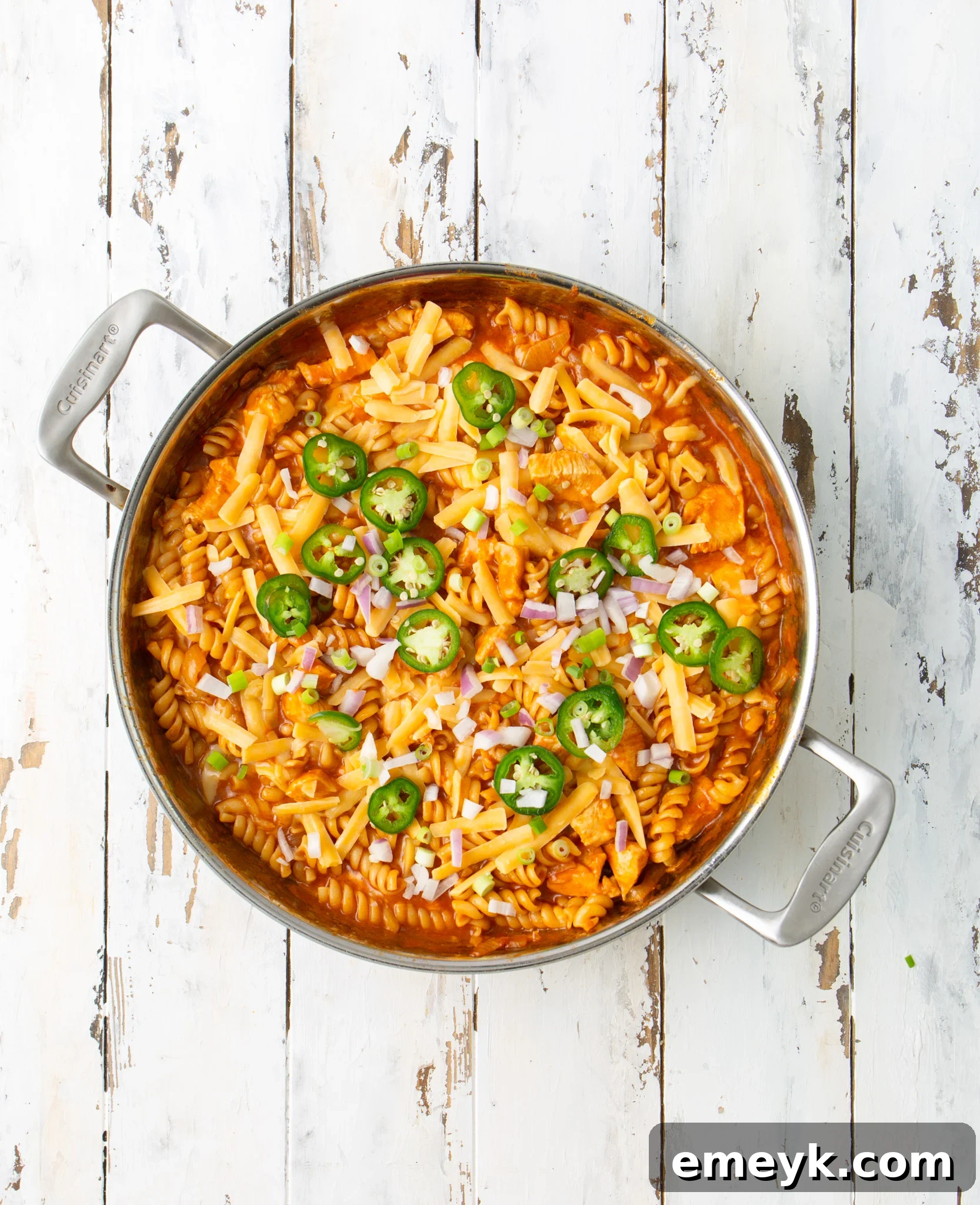 A large silver pot brimming with finished One Pot Chicken Enchilada Pasta, topped with melted cheese and fresh garnishes.