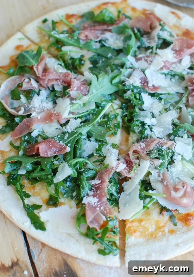 Freshly baked Prosciutto Arugula Pizza on a wooden cutting board, ready to be sliced.