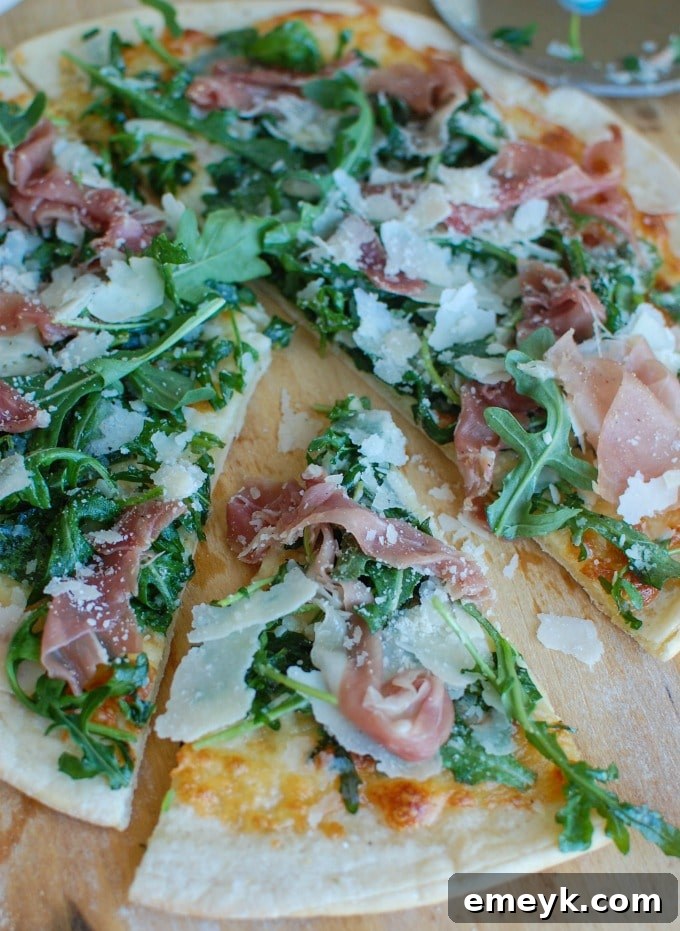 A slice of Prosciutto Arugula Pizza being lifted from a larger pizza, showing the crispy crust and fresh toppings.
