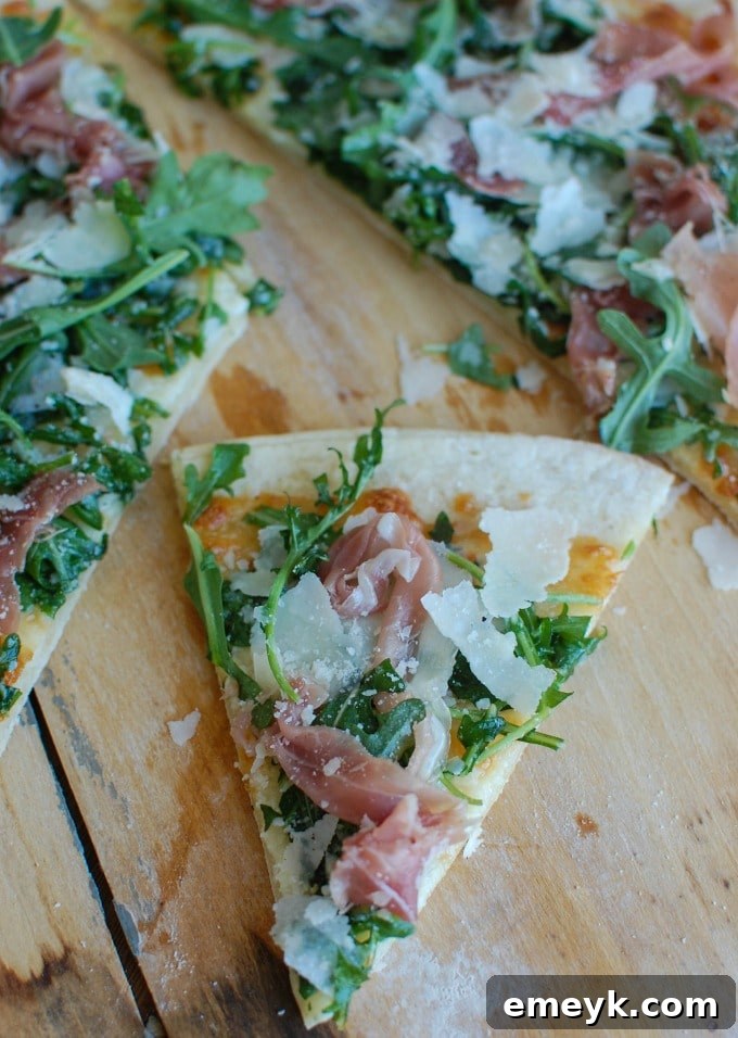 A perfectly cooked slice of Prosciutto Arugula Pizza with visible prosciutto, arugula, and melted cheese.
