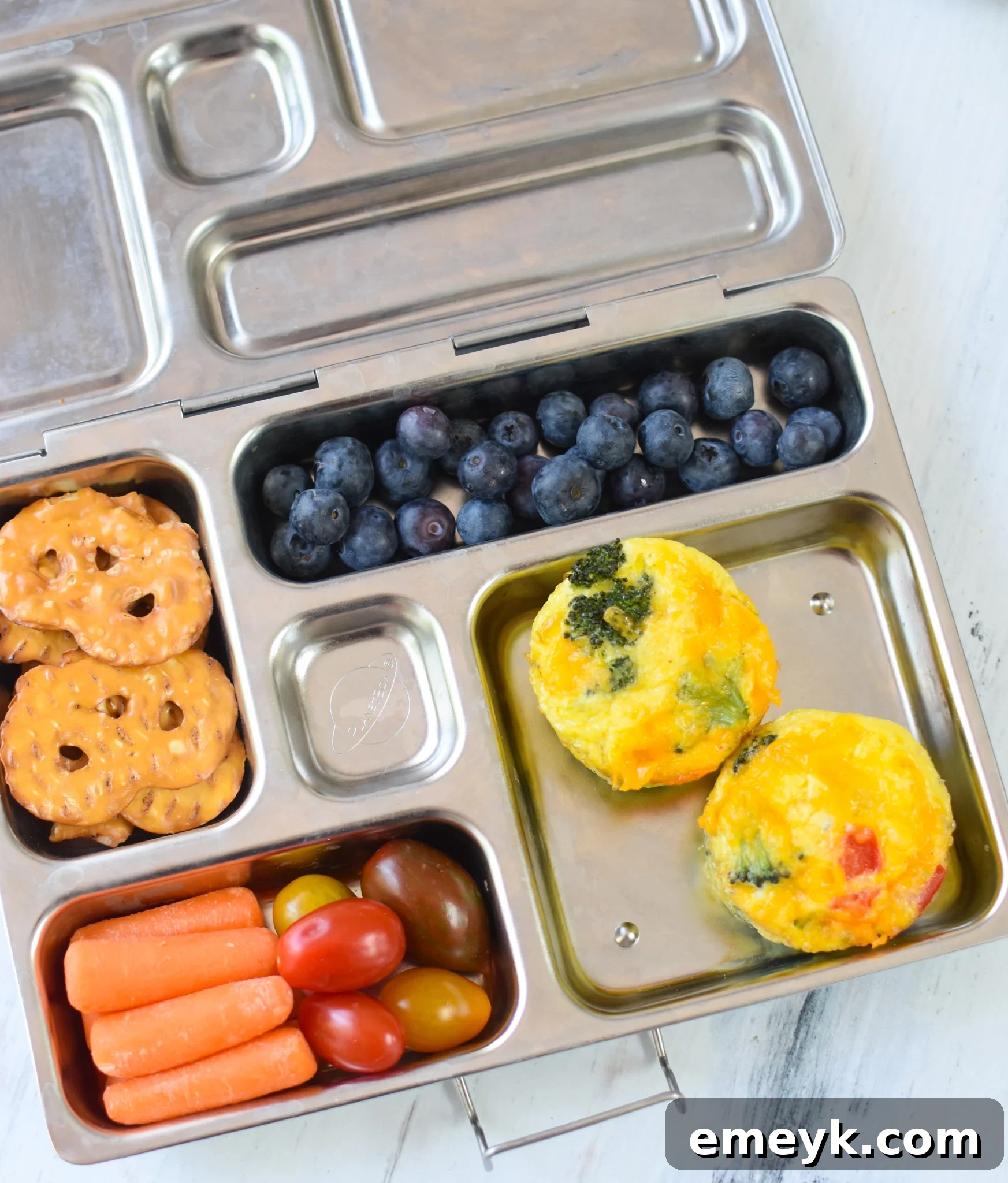Savory Broccoli Cheddar Bites 4 Broccoli Cheddar Cups neatly packed inside a child's lunchbox with fruit and other snacks.