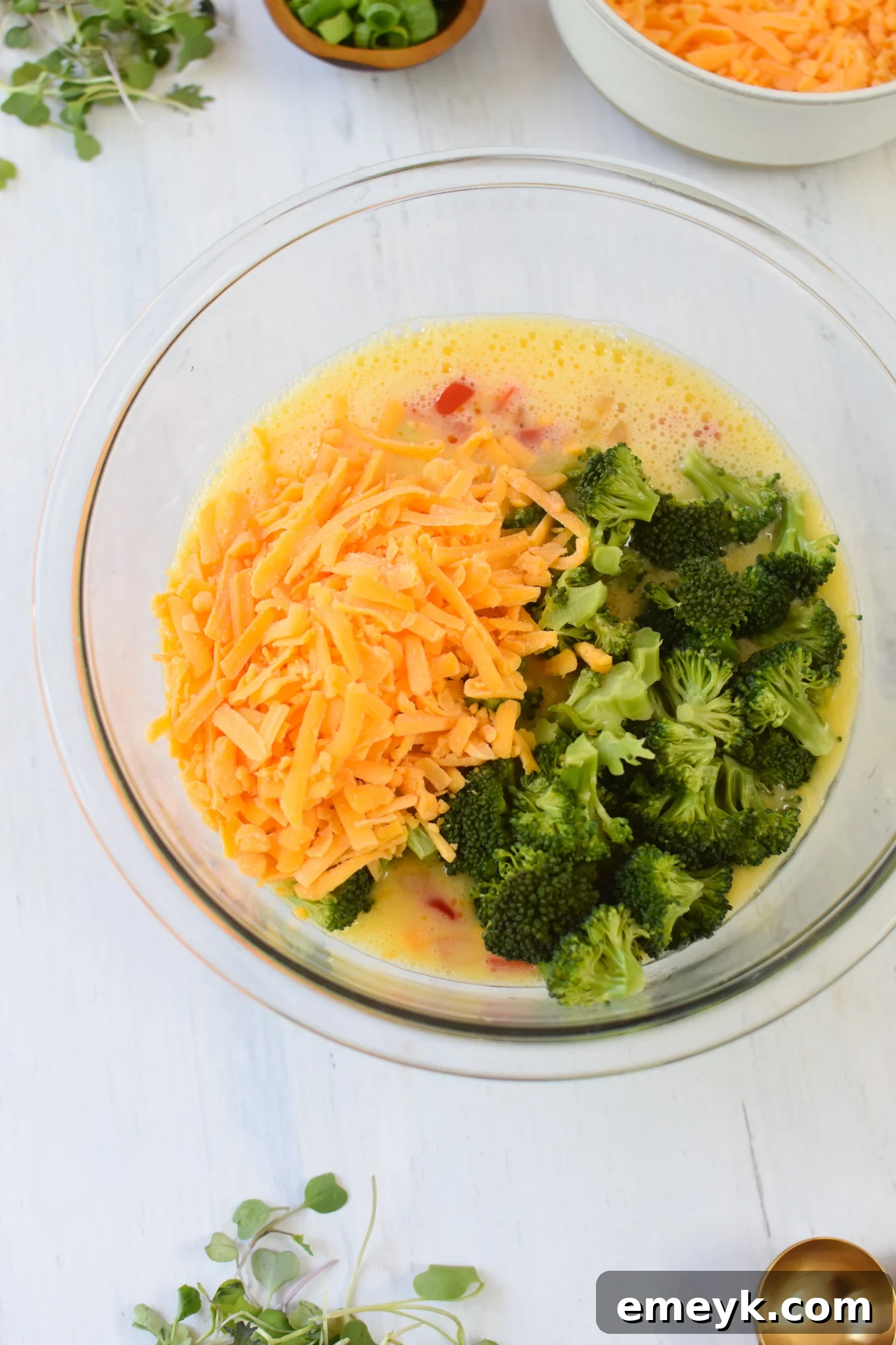 Savory Broccoli Cheddar Bites 9 Broccoli, bell peppers, onions, and cheese mixed into the whisked egg mixture in a large bowl.