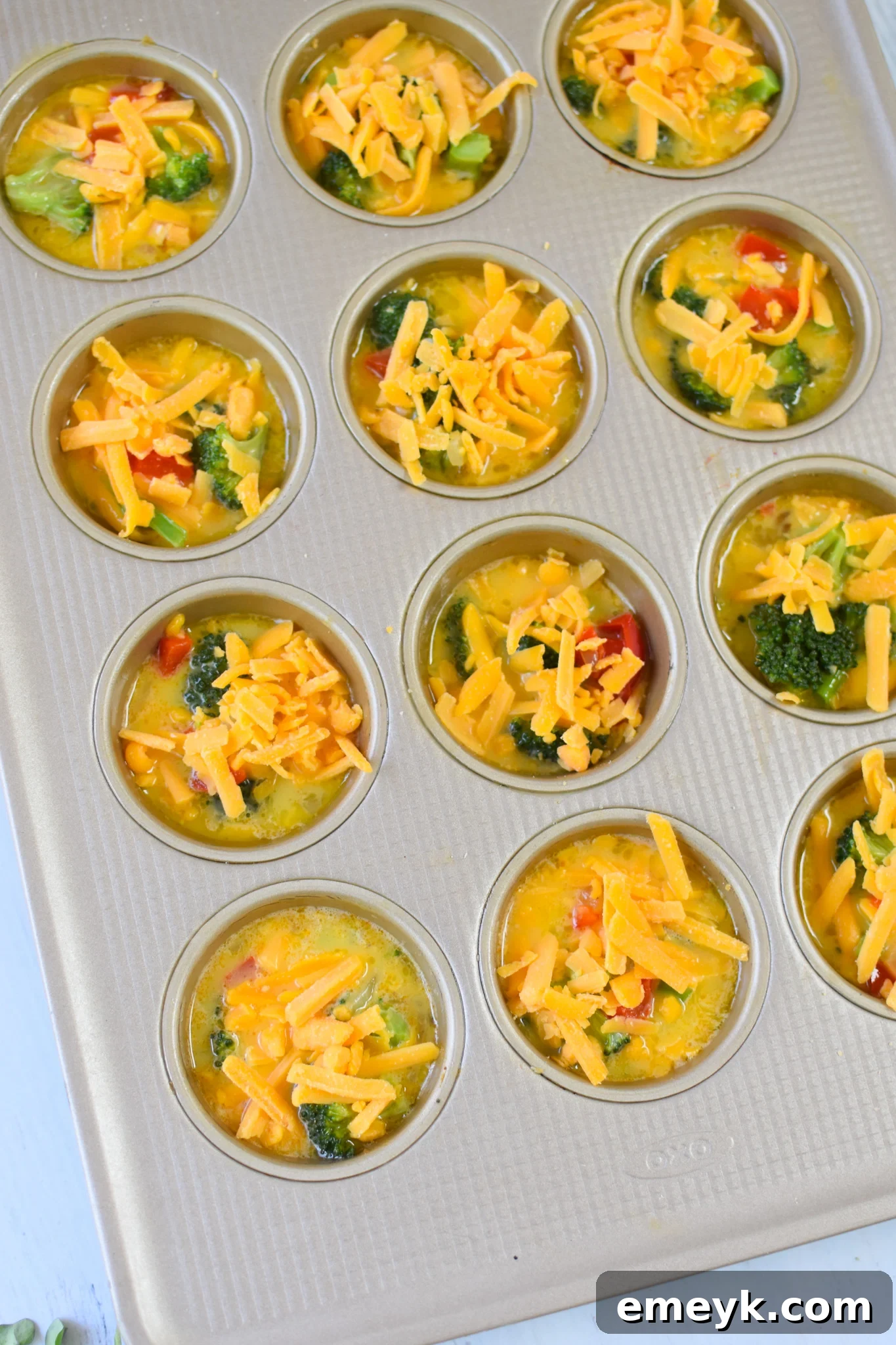 Savory Broccoli Cheddar Bites 10 Egg and vegetable mixture poured into greased muffin tins, ready for baking.