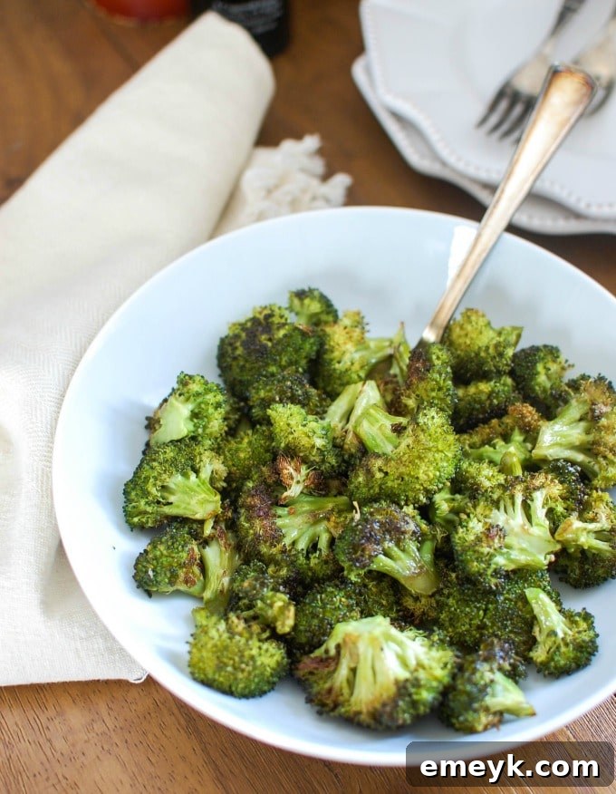 A bowl of perfectly roasted broccoli with a serving spoon, showcasing its slightly charred, crispy edges.